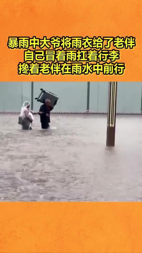 暴雨中大爷将雨衣给了老伴,自己冒着雨扛着行李,搀着老伴在雨水中前行